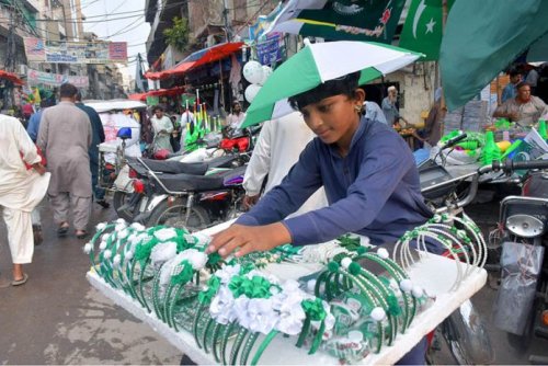 A vendor arranging and displaying national flags, badges and other merchandise related to the 75th Independence Day at Gampat Road Lahore